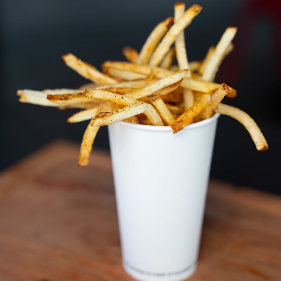 A white cup overflowing with golden, seasoned Smashers french fries on a wooden surface.