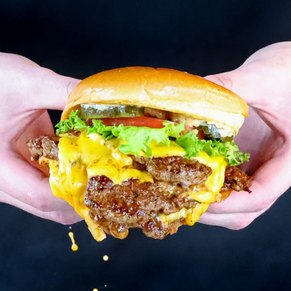 Hands holding a Smashers double cheeseburger with melted cheese, lettuce, tomato, and pickles.