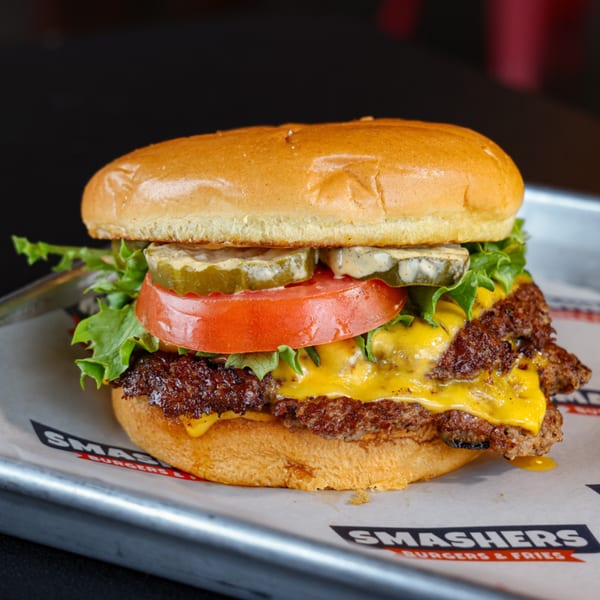 A Smashers double cheeseburger with lettuce, tomato, pickles, and sauce on a brioche bun.