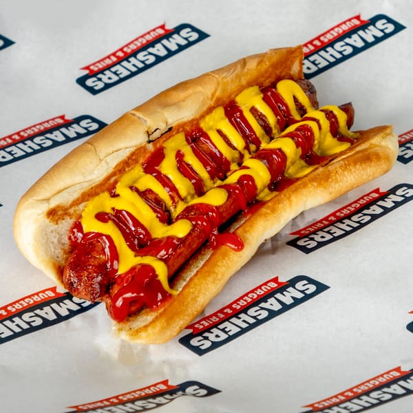 Two hot dogs with ketchup and mustard in a bun on Smashers branded paper.