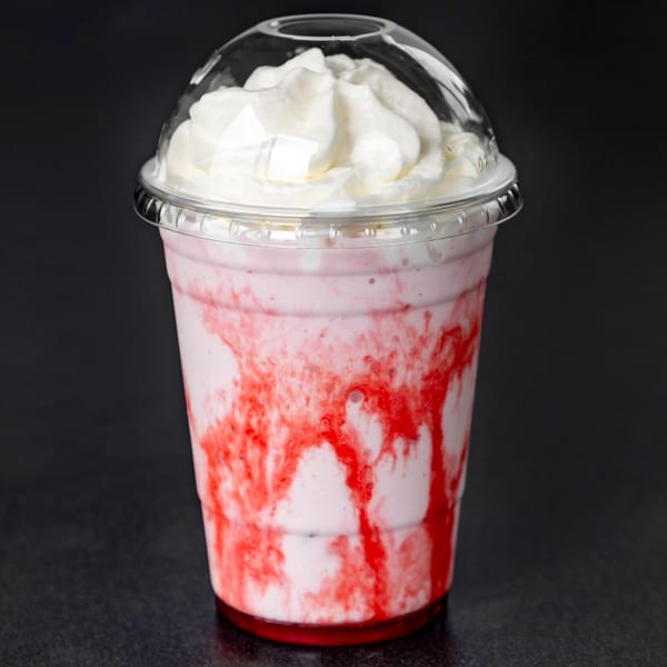 Strawberry milkshake with whipped cream and red syrup swirls in a clear plastic cup.